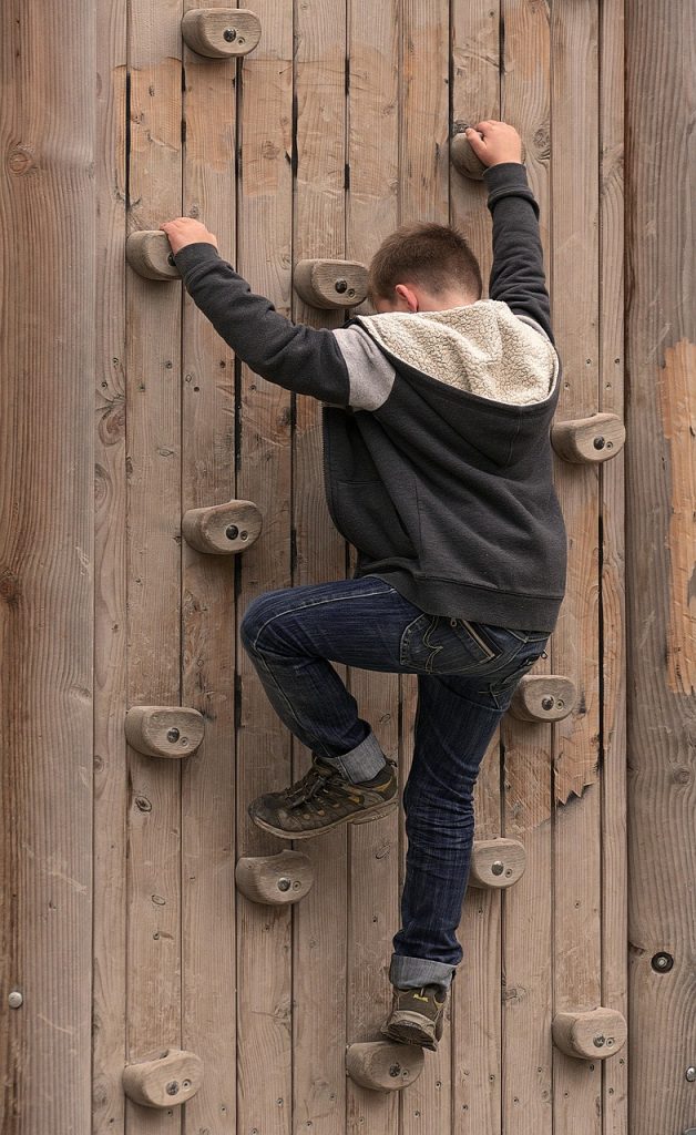 Young boy climbing a wooden wall dotted with climbing holds